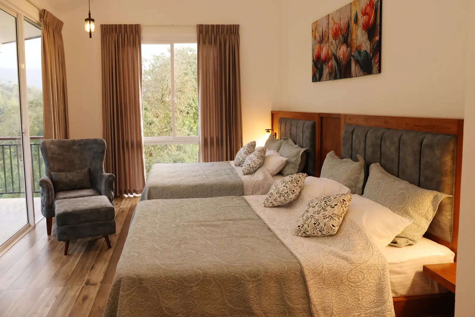 Twin beds with cream floral bedding, grey armchair, and forest views through the balcony