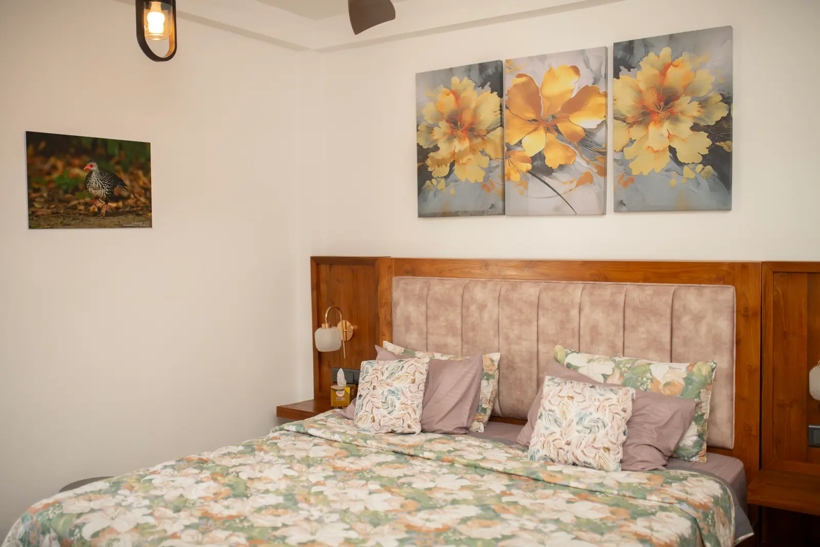 Bed with floral bedding, tufted headboard, and yellow flower wall art