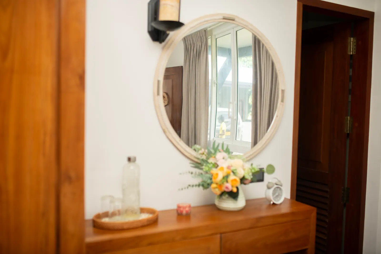 Wooden vanity with round mirror, flowers, and water glasses