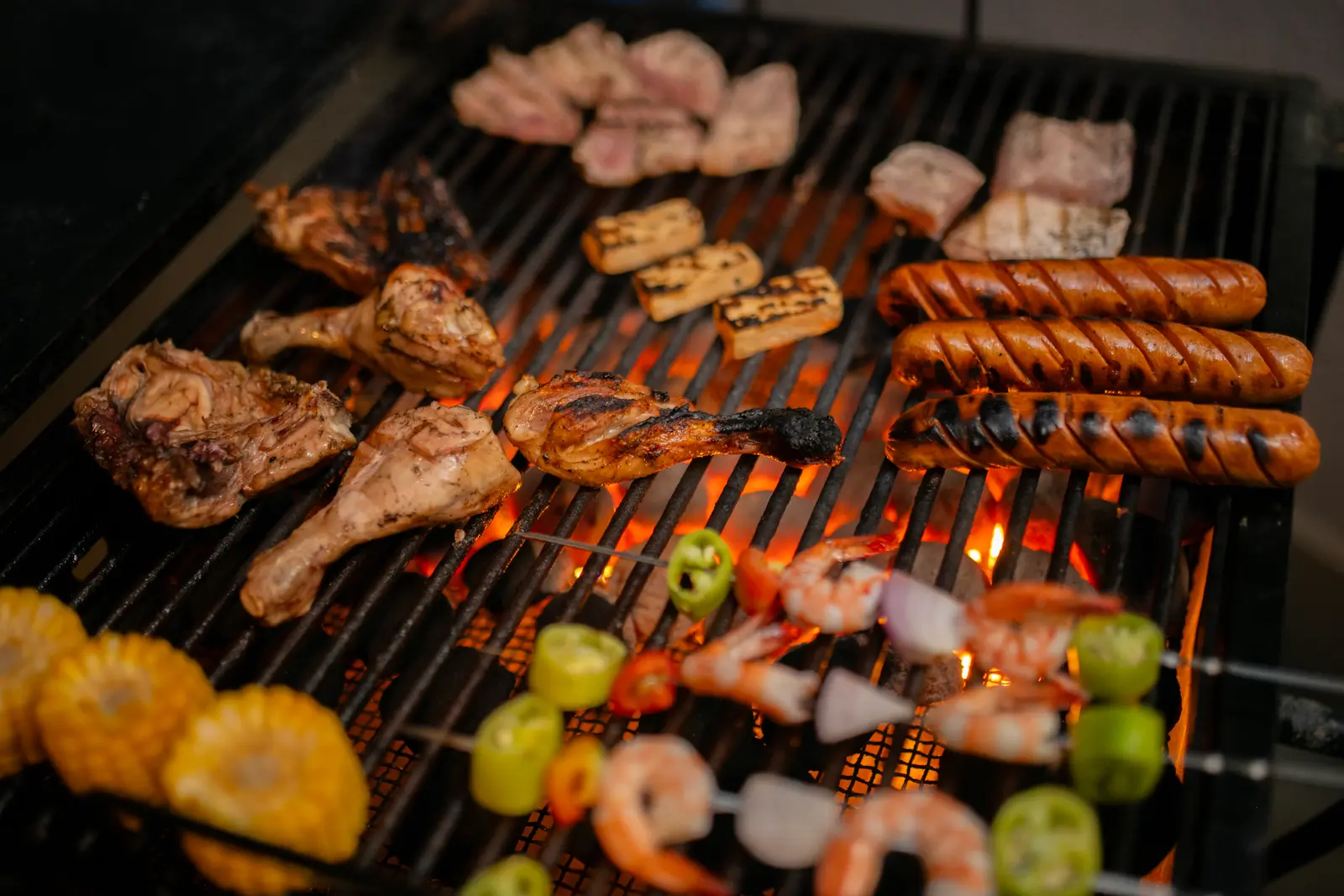 Chicken, sausages, shrimp skewers, and corn grilling over charcoal for a private chef dinner