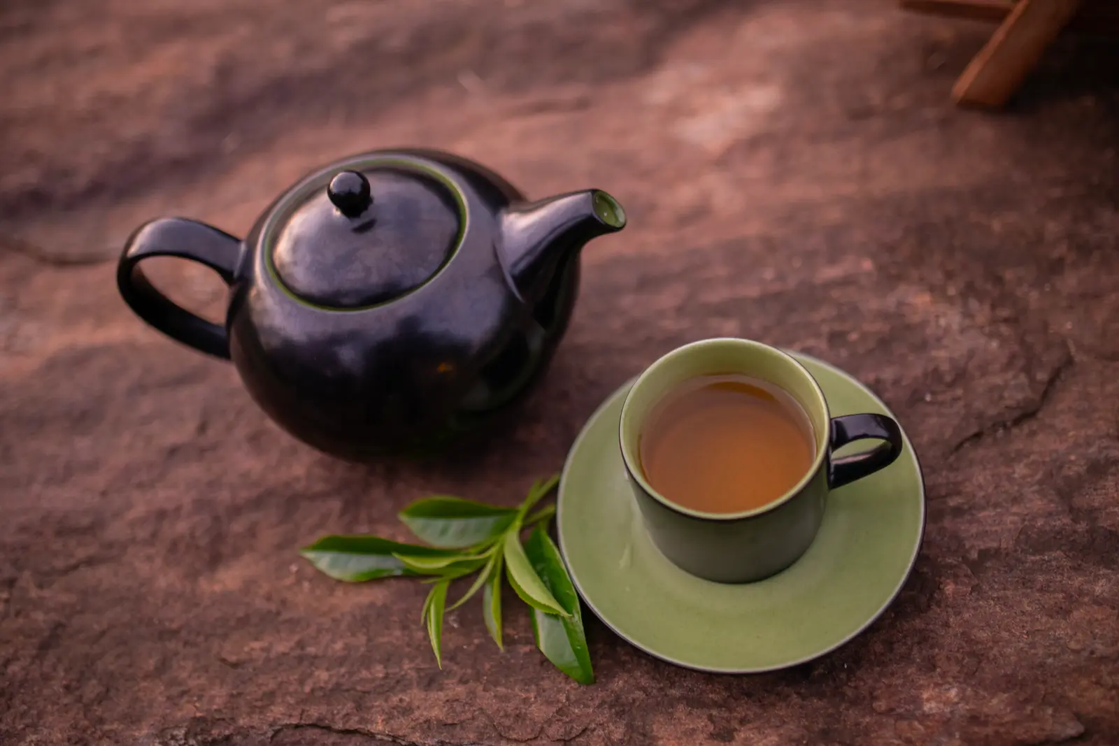 Black teapot and teacup with golden tea and fresh tea leaves on stone, prepared for a private dining experience